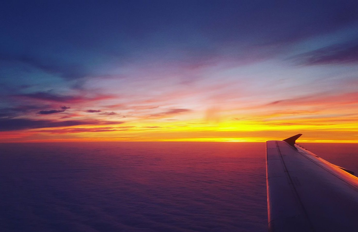 Airplane wing over a sea of clouds at sunset, seen from the window seat